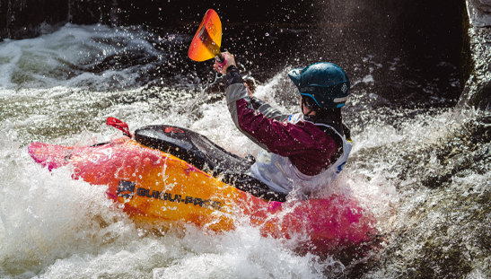 Kayaker navigating whitewater rapids in a bright orange kayak