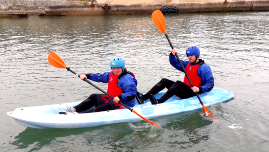 Two beginners paddling a tandem kayak in calm harbour water